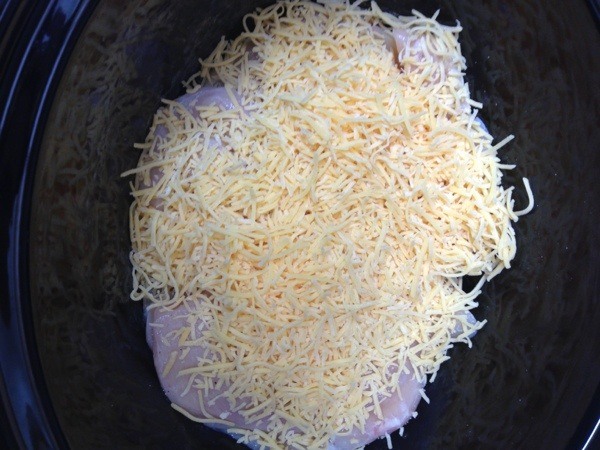 raw chicken in crockpot with cheese on top