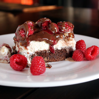 brownie with raspberries and hot fudge on white plate